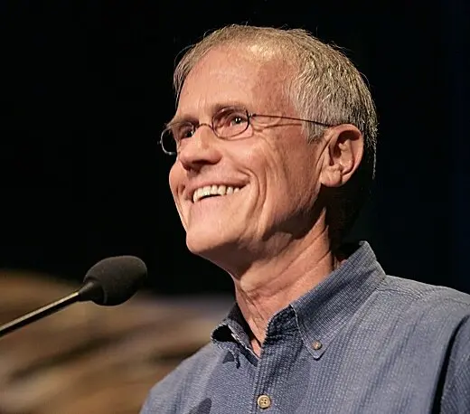 Paul Hawken usando óculos e sorrindo em frente ao microfone durante uma palestra
