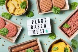 Uma plaquinha escrita: Alimentos plant based e vários destes alimentos, como hambúrguer, massas e grãos.
