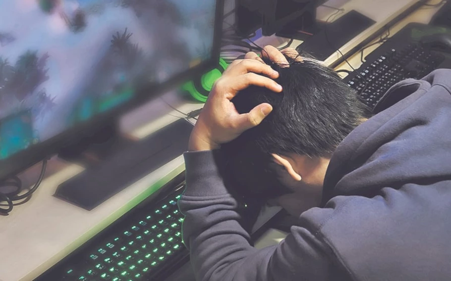 Impactos negativos dos jogos online: um homem sentado de frente a um computador com as mãos na cabeça e rosto abaixado.
