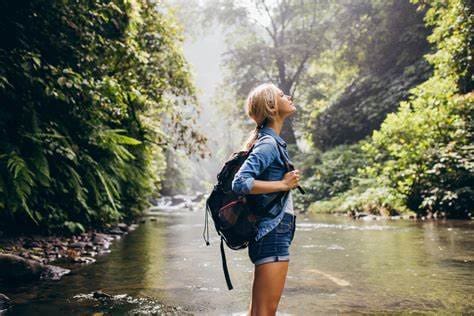Uma adolescente admira a paisagem de uma cachoieira e pensa na sustentabilidade no turismo