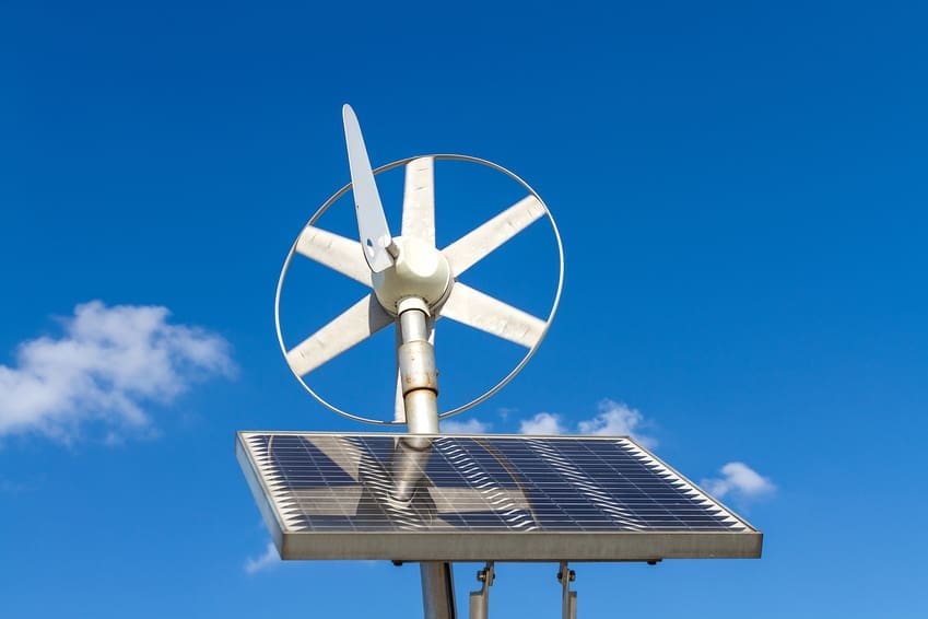 Painel solar e turbina eólica sob um céu azul, representando a geração de energia solar híbrida.