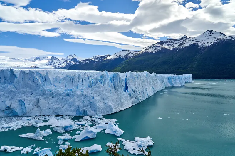 Fotografia de um representante dos glaciares, um grande bloco de gelo em cima de um lago de coloração azul. Ao fundo da paisagem. montanhas com o pico coberto de neve.