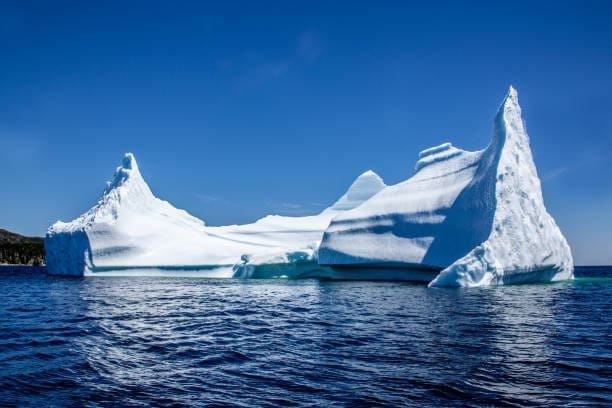 Um imenso iceberg flutua em águas profundas sob um céu azul, revelando apenas a parte visível de sua estrutura gelada acima da superfície do oceano.
