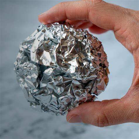 Uma mão segurando uma bola de papel alumínio, representando a Reciclagem de alumínio
