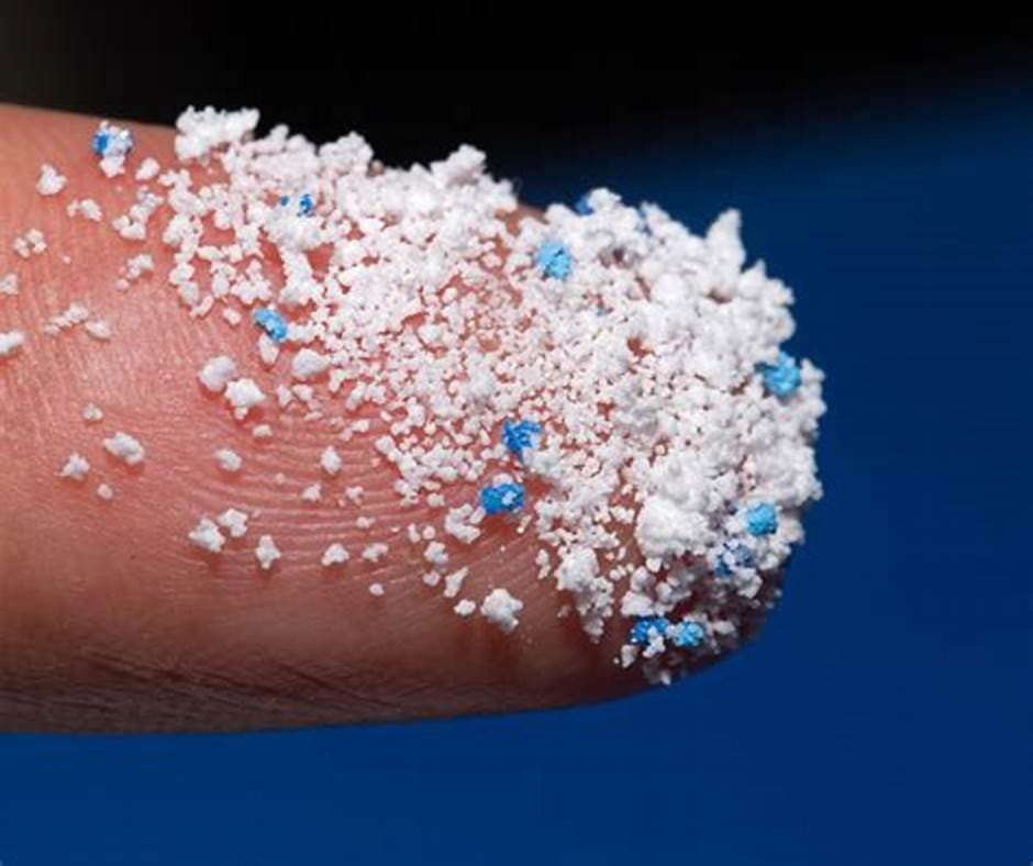 Um dedo com pequenos microplásticos brancos e azuis