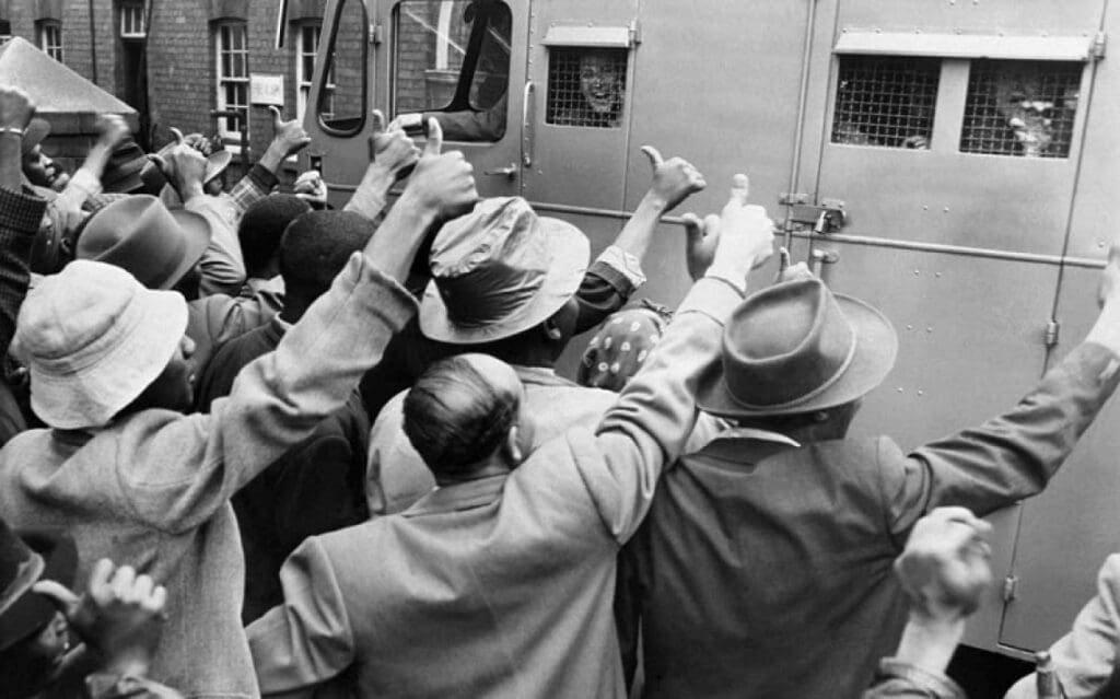 A segregação social representada em uma fotografia, várias pessoas em uma estação de trem com a plataforma e trem lotados de pessoas.