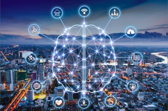 Fundo da imagem uma cidade a noite com desenho de um cérebro digital conectado a vários símbolos do cotidiando, representando Internet das Coisas (IoT) – conectando dados de forma inteligente.