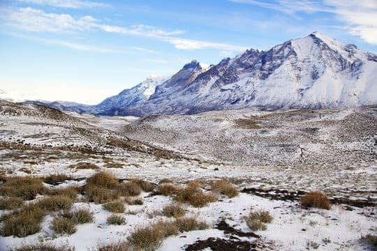 Bioma Tundra: vegetação rasteira e dispersa, solo coberto com neve, ao fundo da imagem montanhas cobertas por gelo.