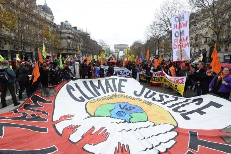 muitas pessoas em evento na rua apresentam uma enorme faixa escrito justiça Climática em inglês e protesta sobre a injustiça.