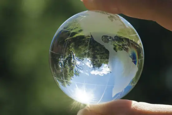 Uma imagem de um globo terrestre vendo segurado na ponta dos dedos e refletindo uma floresta, onde ocorrem os ciclos naturais.