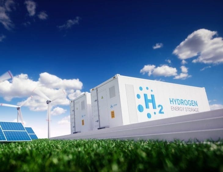 Cointerner escrito hidrogênio verde em um campo juntamente a placas solares e turbinas eólicas.