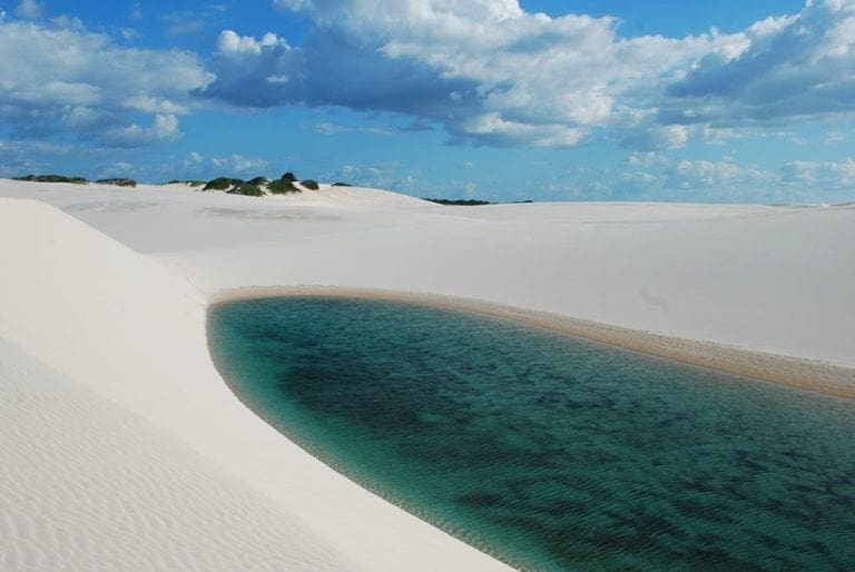 Dunas costeiras sob luz do sol, mostrando areia branca moldada pelo vento.