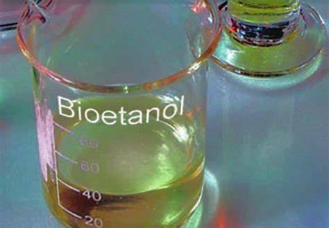 Um béquer de vidro transparente contendo bioetanol com coloração amarelo em seu interior em cima de uma mesa.