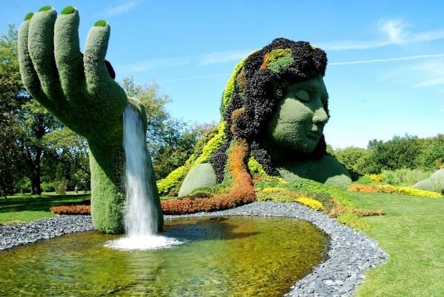 Arte no Jardim Botânico de Montreal: uma escultura de pedra com o rosto de uma mulher e as plantas formam seu cabelo, sua mão emerge de um lago artificial.