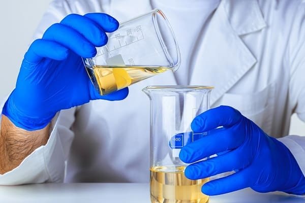 Um cientista em um laboratório com luvas azuis, move o formol de um recipiente para o outro.