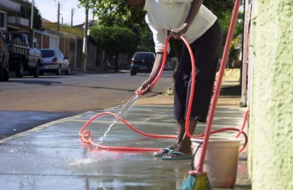 uma senhora lavando a calçada sem pensar no desperdício de água