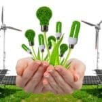 Imagem sobre energia sustentável mostrando mãos segurando lâmpadas ecológicas com textura de plantas, cercadas por painéis solares e turbinas eólicas ao fundo.